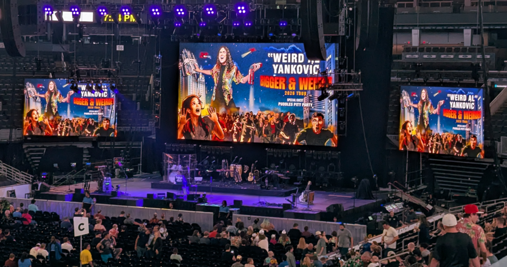 The stage at TD Garden with three big screens showing "Weird Al's" Bigger & Weirder Tour poster